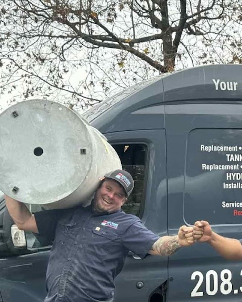 Tyler Case, founder and master plumber of Water Heaters Unlimited — holding an old water heater tank in front of the company van
