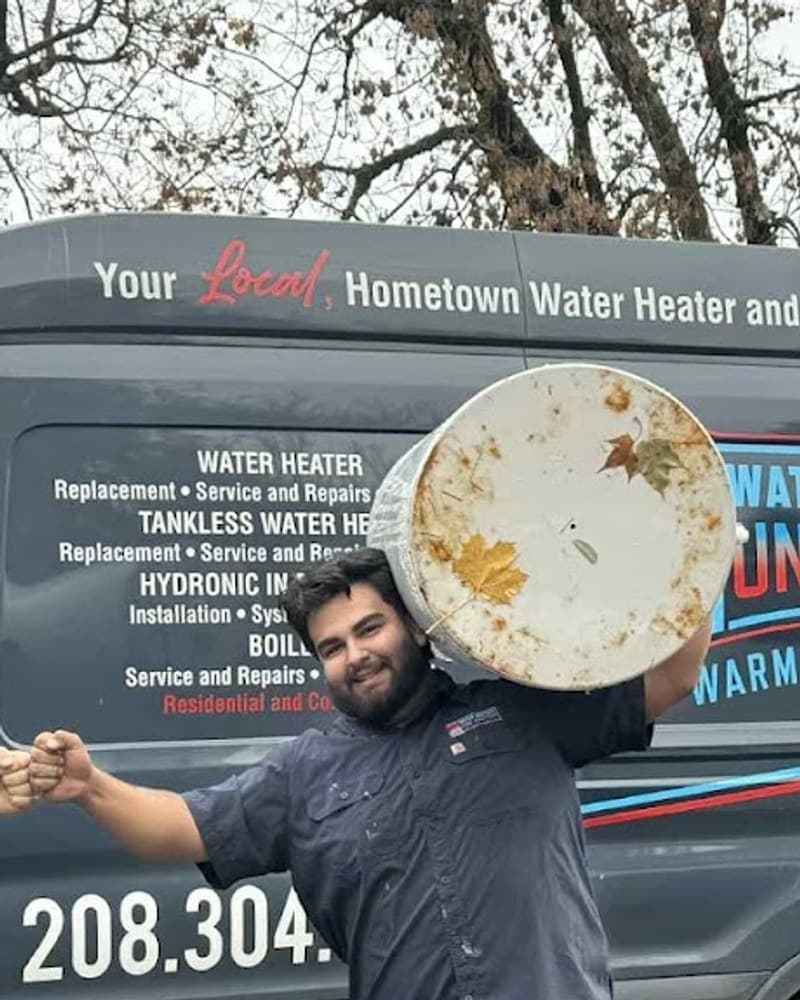 Tyssen Case, co-owner and lead technician of Water Heaters Unlimited — holding a rust-stained water heater tank in front of the company van